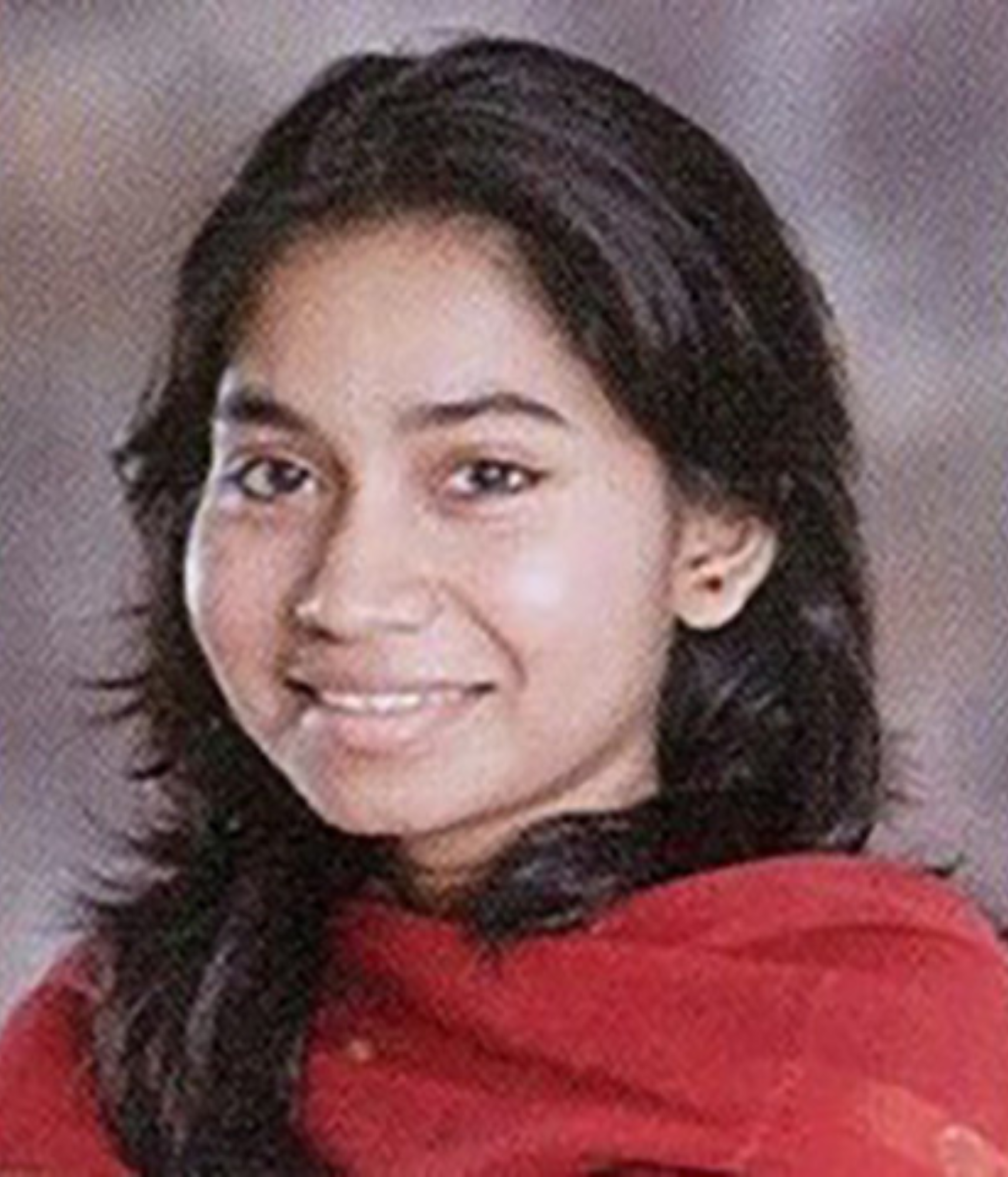 A person with long dark hair smiles softly, wearing a red shawl against a blurred background.