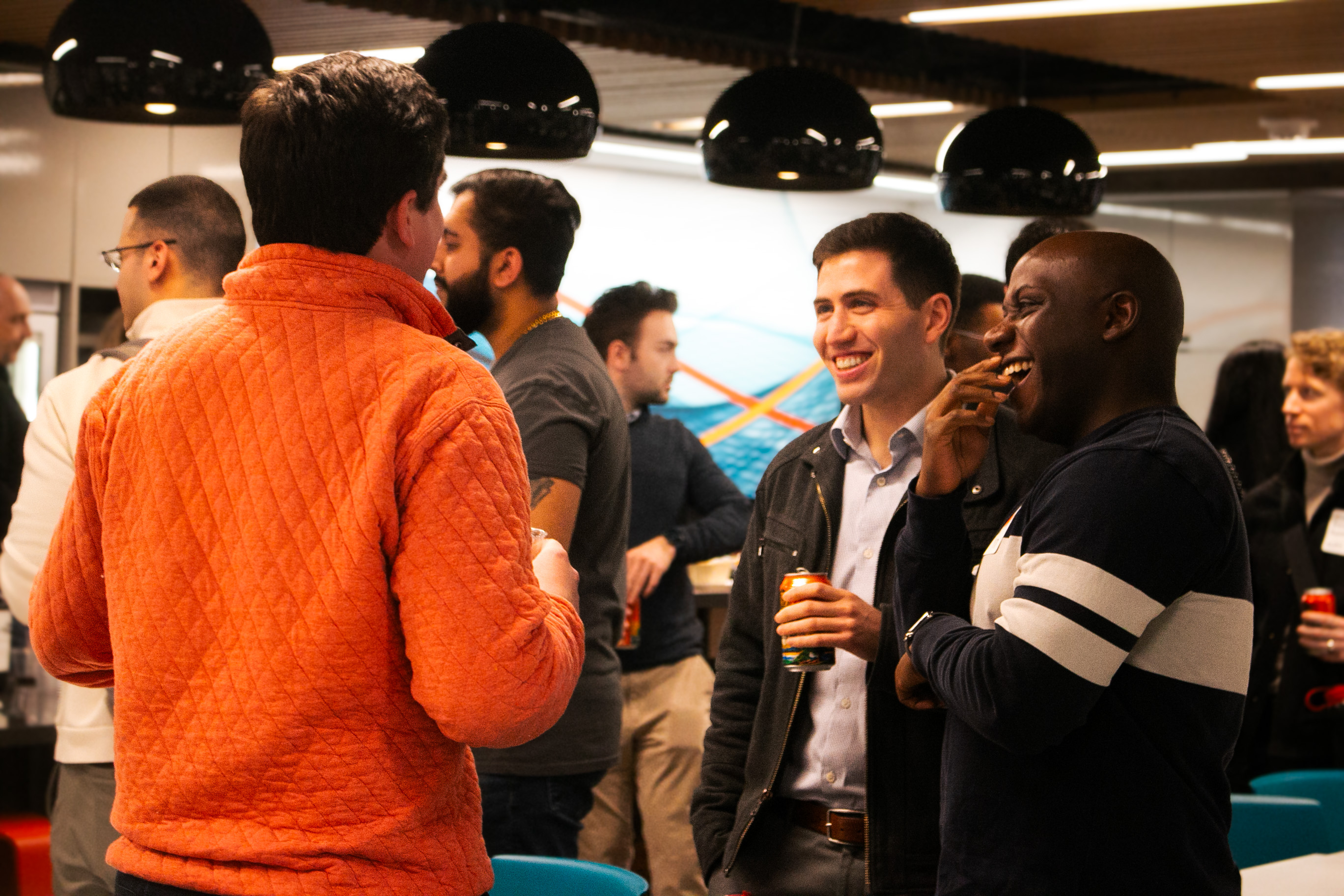 A group of people in casual attire engaged in conversation at a social gathering, surrounded by a modern, colorful backdrop.
