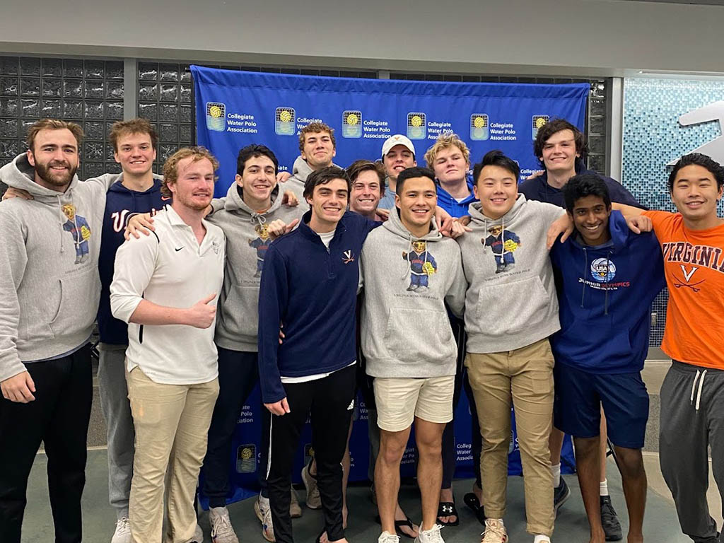 A group of young men in casual clothing pose together in front of a blue backdrop featuring logos, smiling and celebrating.