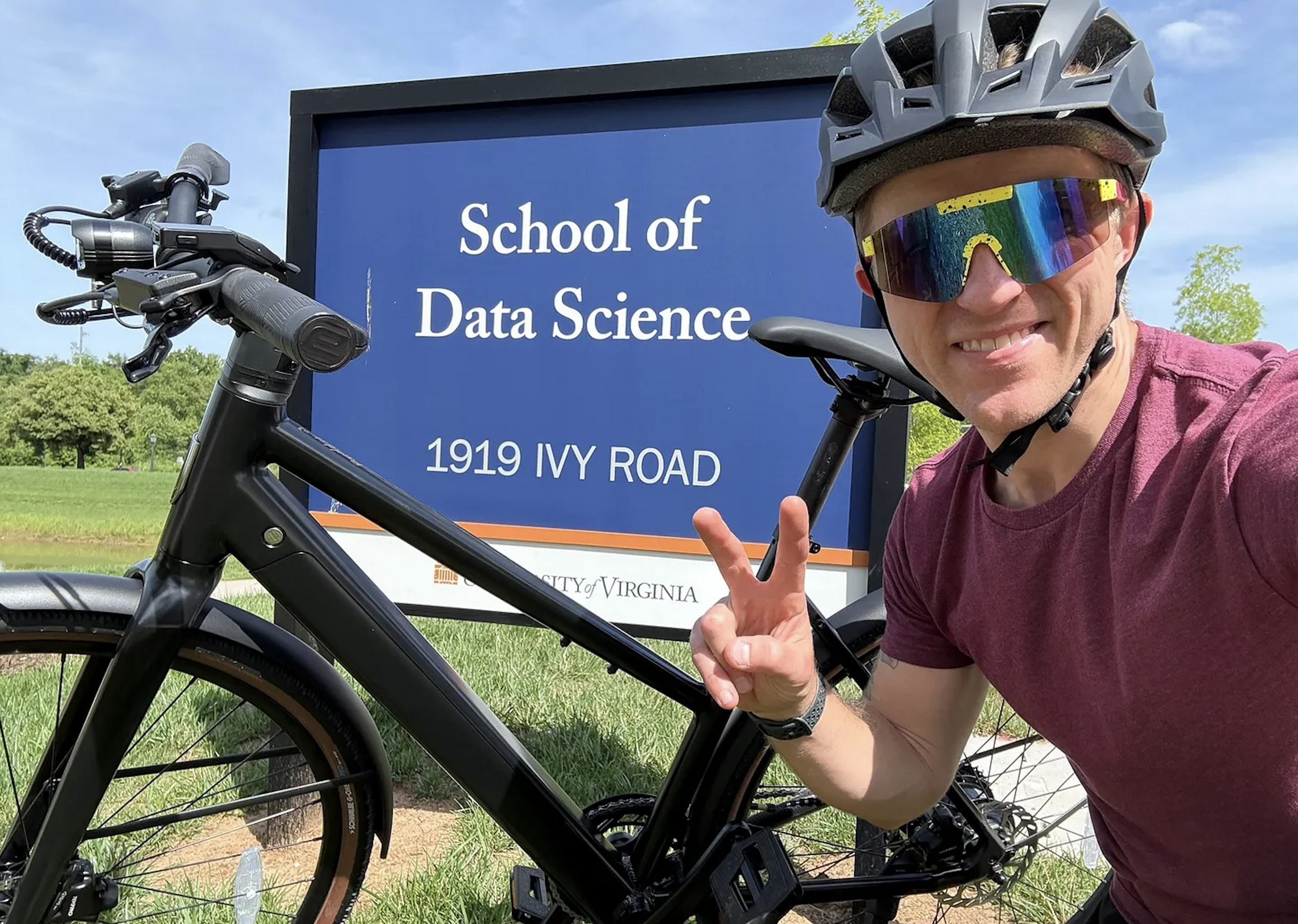 Professor Stephen Turner poses in front of the School of Data Science sign with his bike, wearing his bike helmet. 