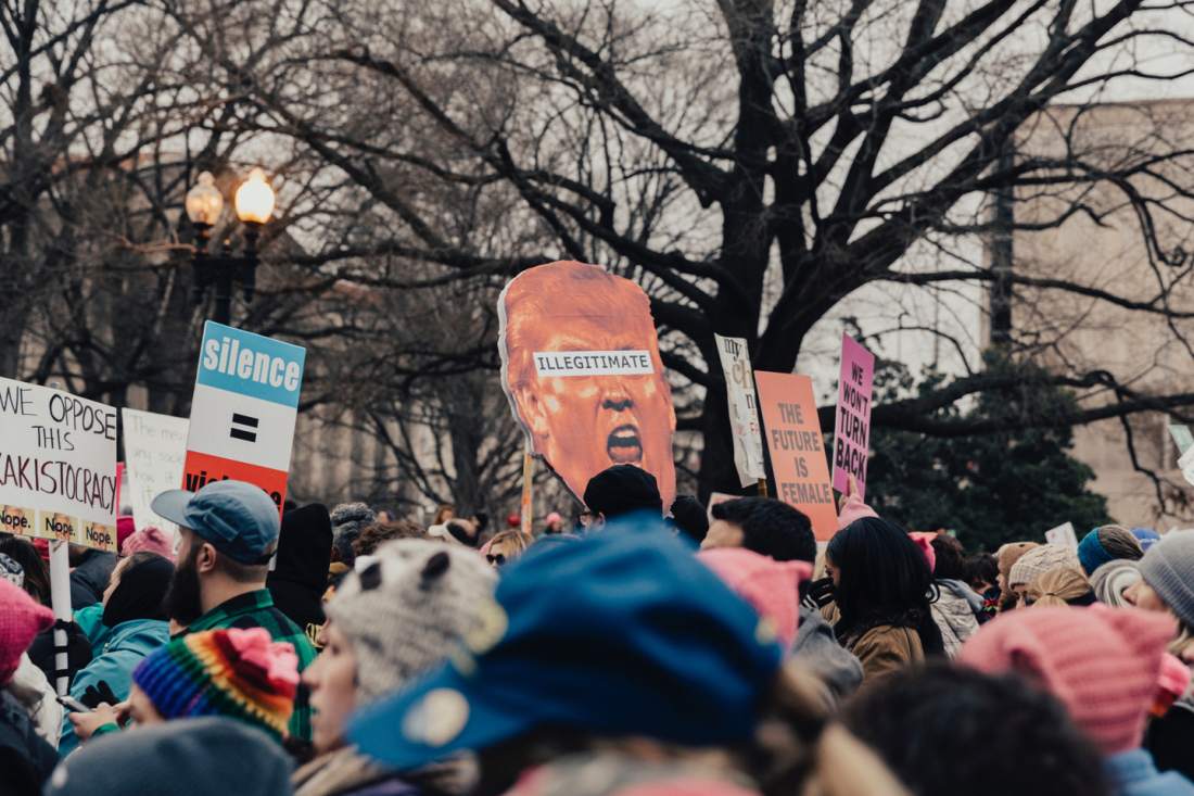 A crowd at a protest holding signs, including a large caricature with the word "illegitimate."