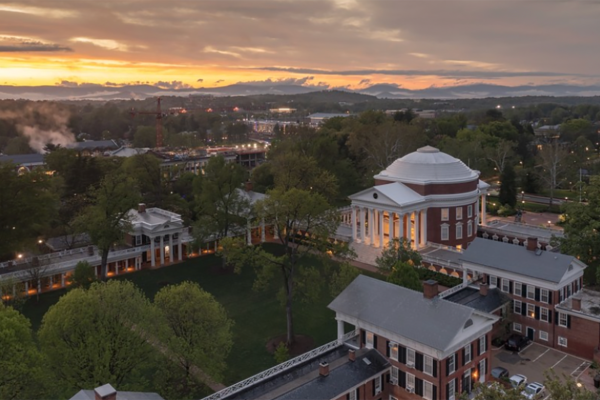 Aerial view of a university campus at sunset, featuring a domed building with columns surrounded by trees. The sky is a mix of orange and gray.