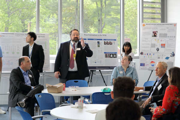 A group of professionals engaged in discussion around research posters in a bright, modern conference room setting.