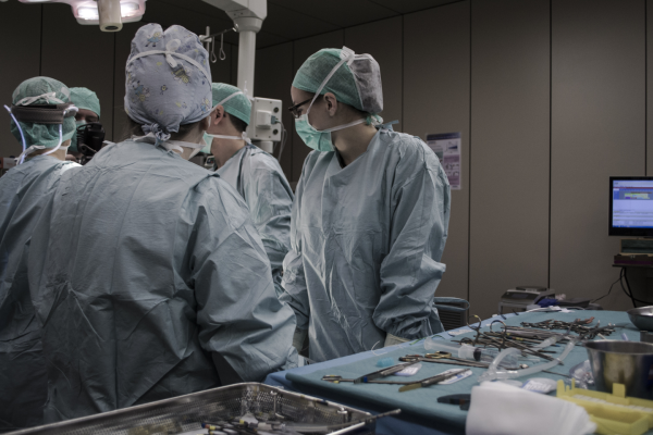 A team of surgeons in blue scrubs and masks in a sterile, dimly lit operating room. Medical instruments neatly arranged on trays.